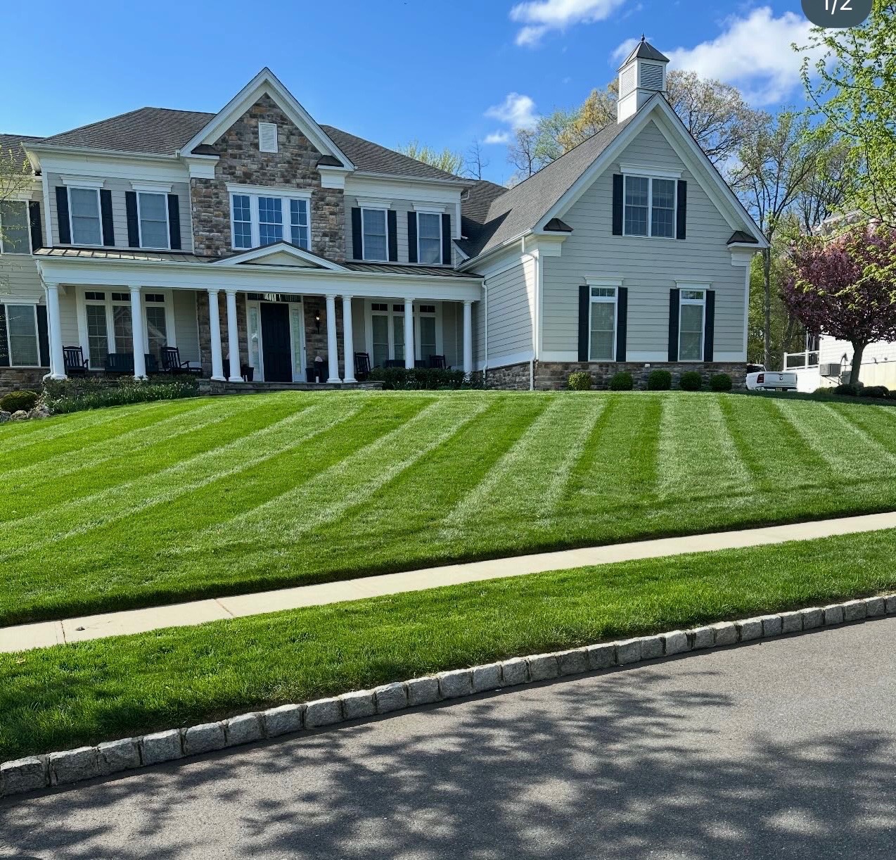 Beautifully manicured striped lawn in front of a large stone and siding home